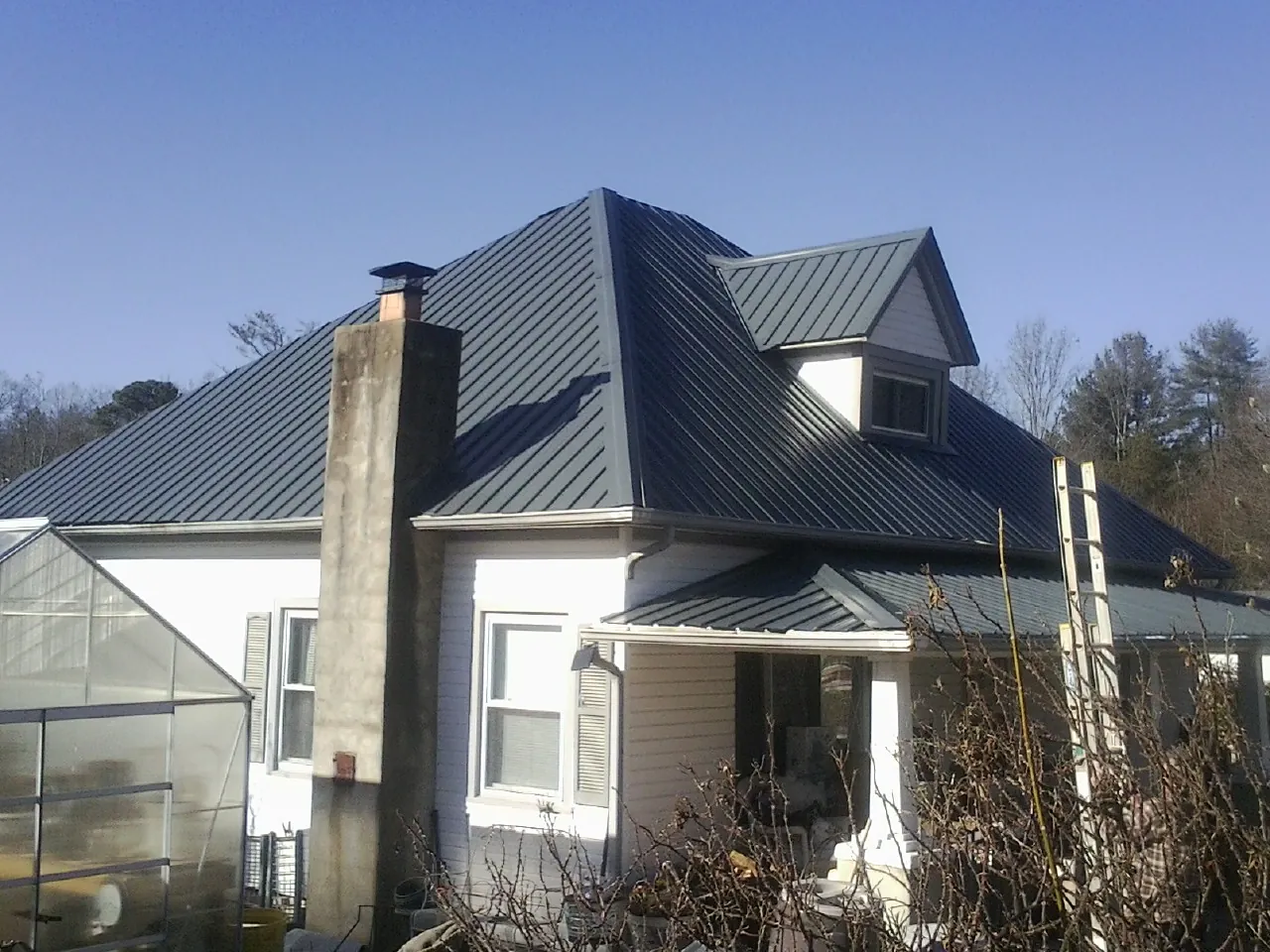 Dark blue standing seam metal roof on a white farmhouse with dormer — Slate & Tile Roof Repair by Roofing Brothers in Wapanucka
