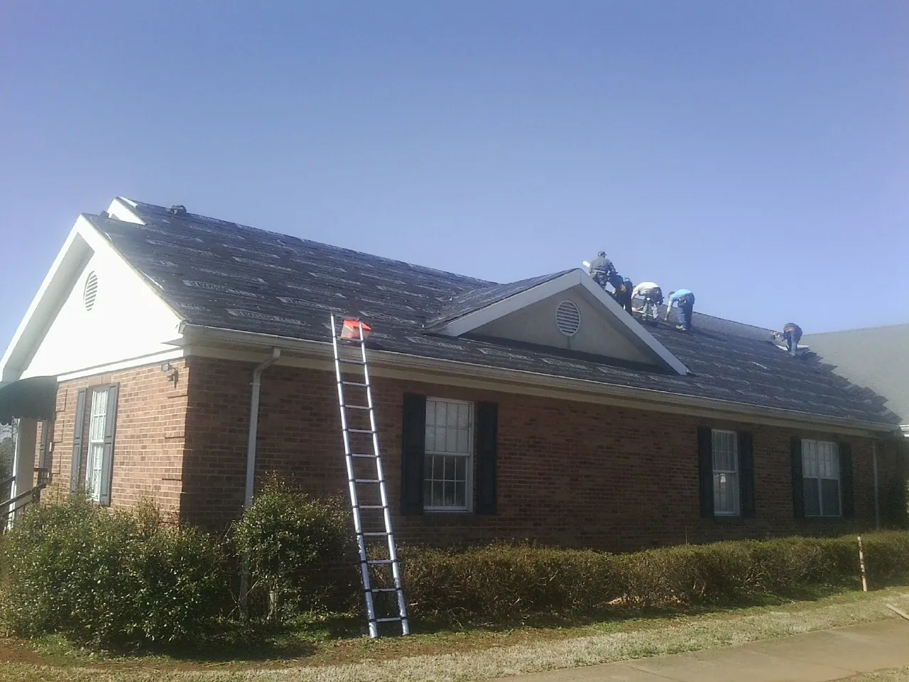 Crew tearing shingles off a brick ranch roof with a ladder set — Emergency Roof Repair work by our crew in Wapanucka