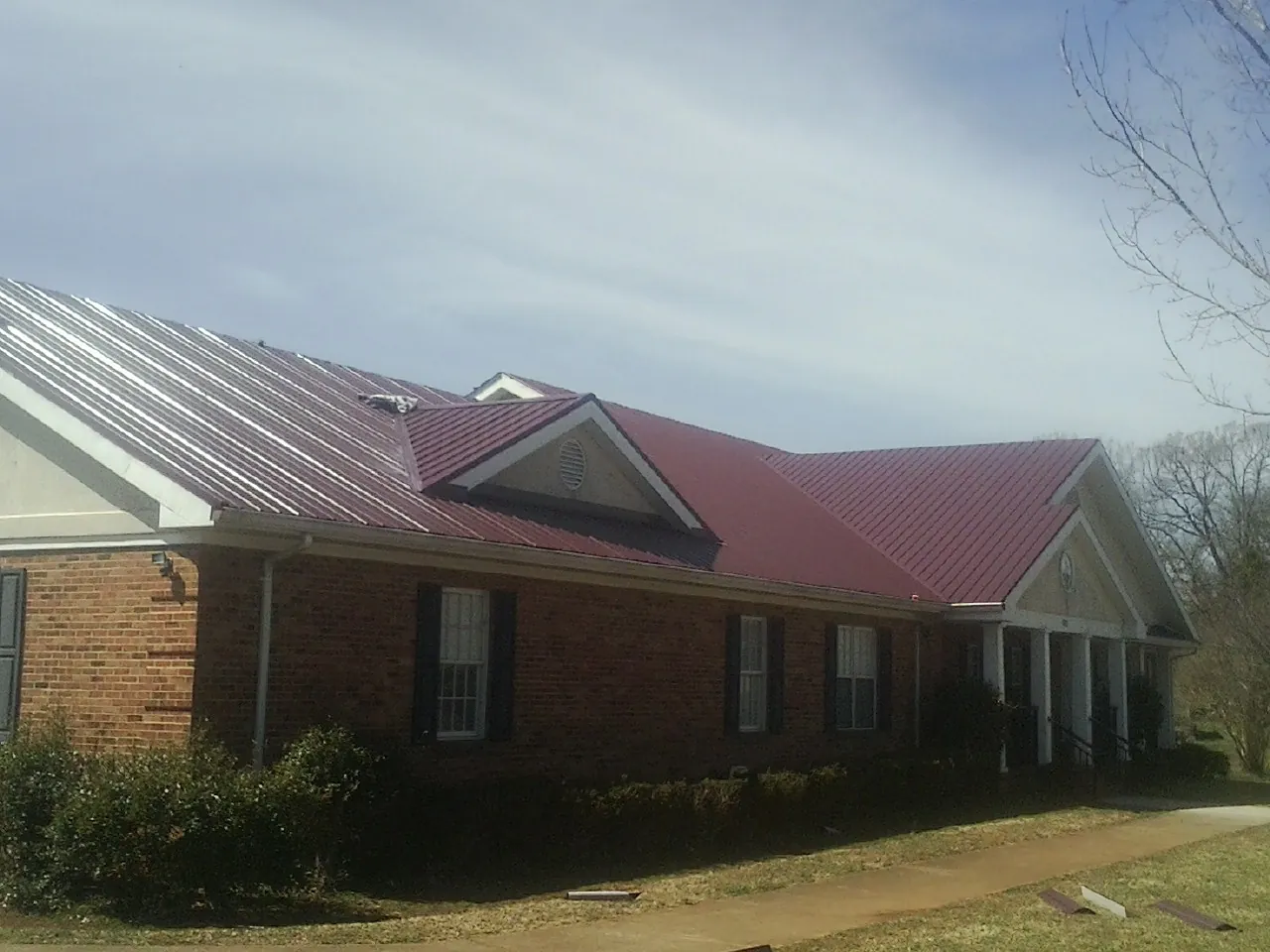 Red metal roof with gabled entries on a long brick building, from a Hail Damage Roof Repair job in Wapanucka