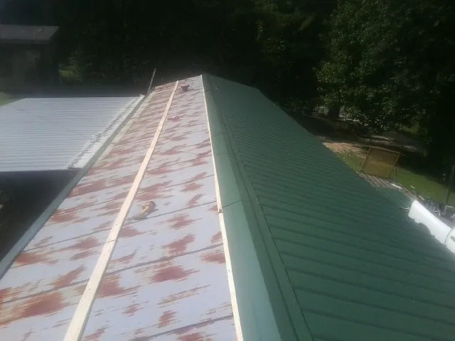 Old rusted panels beside newly installed green metal roofing — Wind Damage Roof Repair by Roofing Brothers in Wapanucka