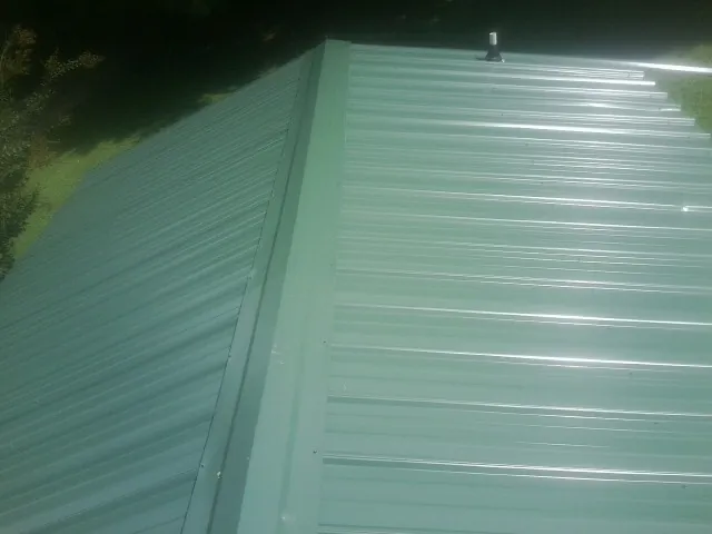 New green metal panels meeting at the ridge of a roof — Flat Roof Repair work by our crew in Wapanucka