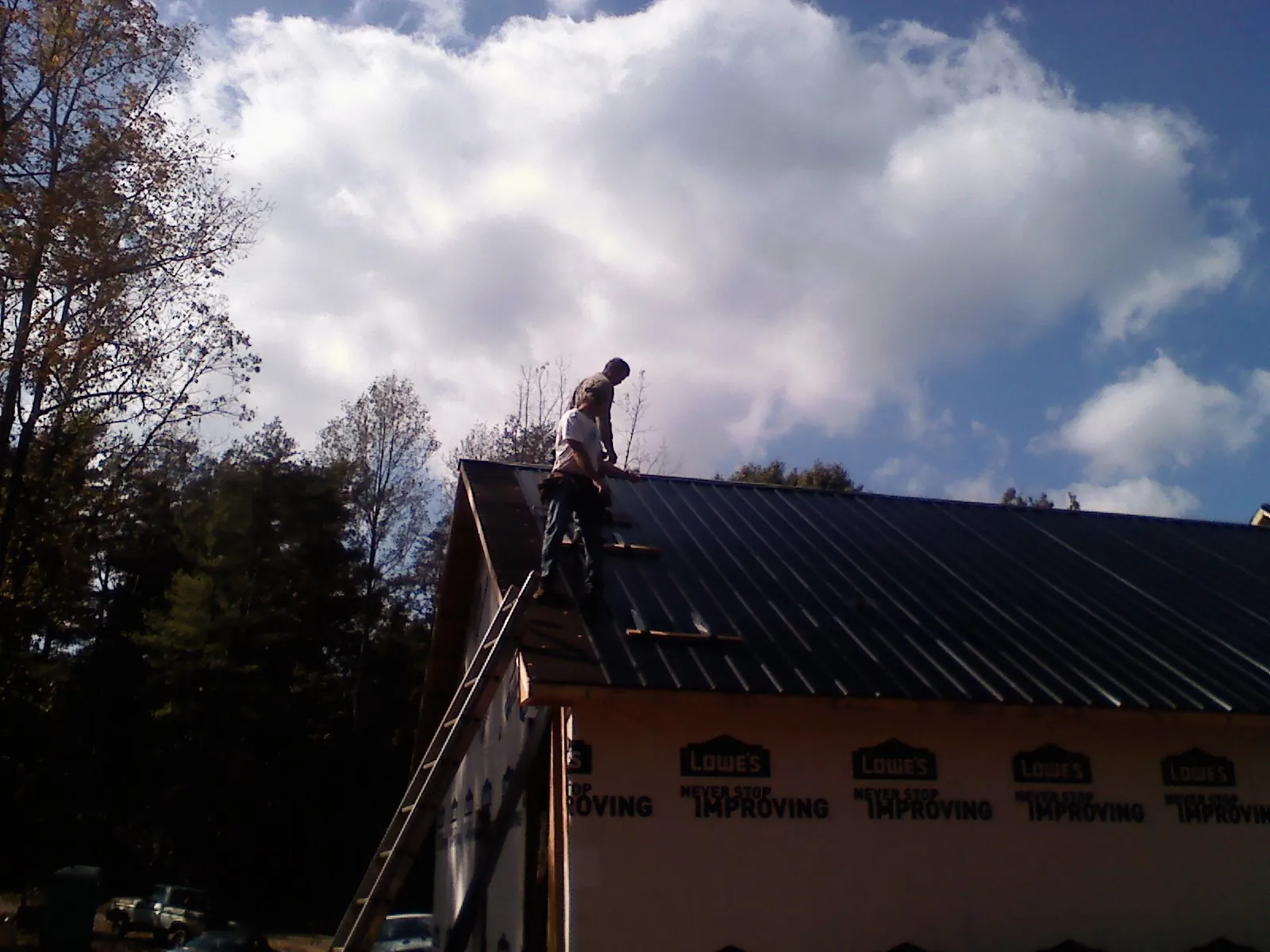 Roofer fastening dark metal panels high against a cloudy sky, from a Roof Inspection job in Wapanucka