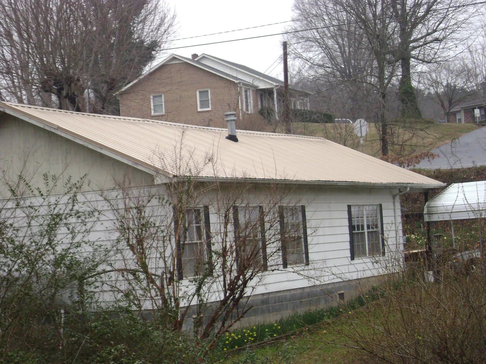 Tan metal roof on a white sided house set into a hillside — Commercial Roofing by Roofing Brothers in Wapanucka